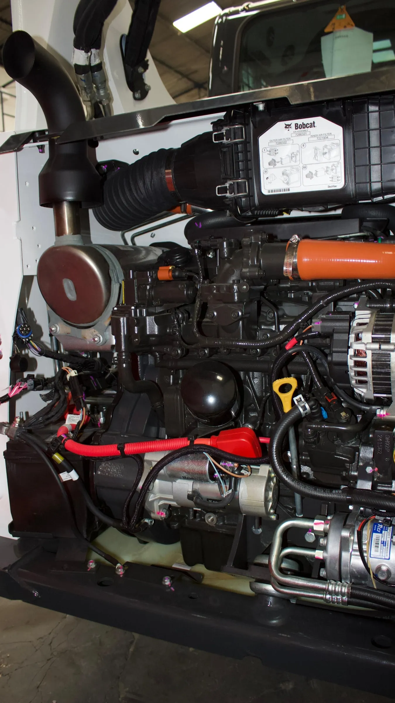 Foto vertical: motor de un minicargador Bobcat con el capó abierto